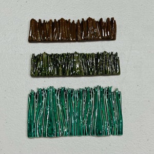 May include: Three different types of green and brown grass borders for model railroading or miniature landscaping. The borders are made of a textured plastic material.