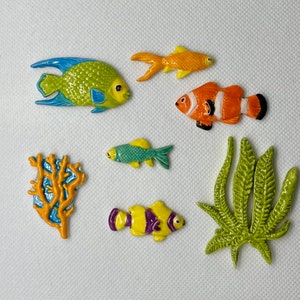 May include: A set of colorful ceramic sea life figurines, including a blue and green angelfish, an orange and white clownfish, a yellow and orange fish, a green seaweed, and an orange coral.