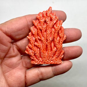 Puede incluir: Una escultura de coral de cer&aacute;mica de color coral con una superficie detallada y texturizada. La escultura tiene la forma de un grupo de ramas de coral.