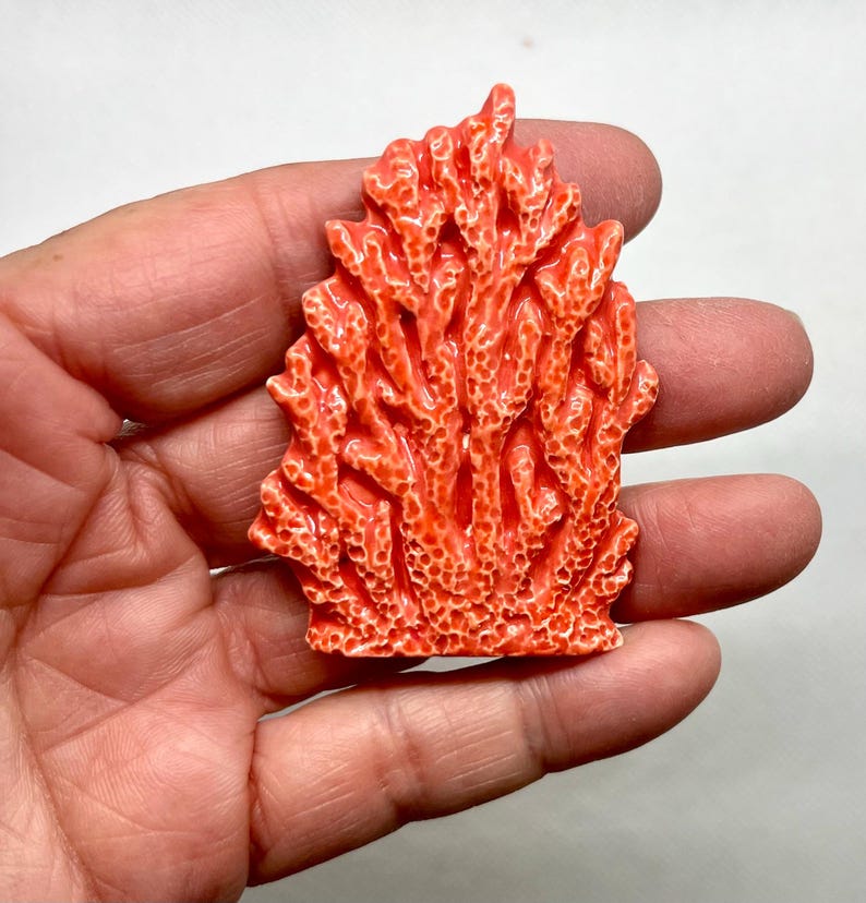 Puede incluir: Una escultura de coral de cer&aacute;mica de color coral con una superficie detallada y texturizada. La escultura tiene la forma de un grupo de ramas de coral.