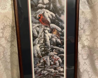 May include: Framed print of a winter scene with cardinals and chickadees perched on a snow-covered pine tree. The birds are red, gray, and white, and the background is a soft blue.