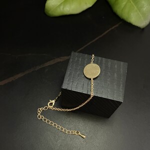 Könnte beinhalten: Ein goldenes Kettenarmband mit einem großen, runden, goldenen Anhänger. Das Armband wird auf einer schwarzen Schachtel präsentiert.
