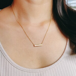 May include: A delicate gold chain necklace with a small, rectangular bar pendant featuring a white opal inlay.