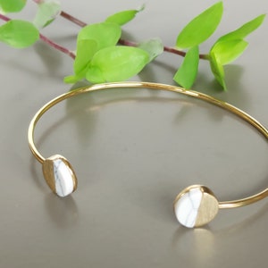 May include: A gold bangle bracelet with white marble accents. The bracelet is open and has a simple design.