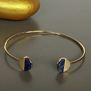 May include: A gold bangle bracelet with two half-circle lapis lazuli stones.