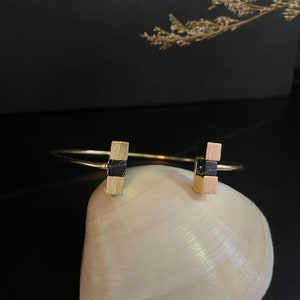 Op de afbeelding: Een gouden armband met zwarte marmer accenten. De armband is open en heeft een eenvoudig ontwerp.