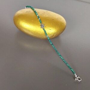 May include: A green malachite beaded bracelet with a silver turtle charm. The bracelet is on a gold-coloured rock.