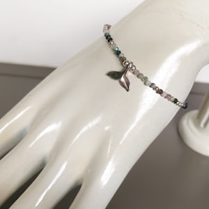 Op de afbeelding: Een delicate armband met een zilveren walvisstaartbedel. De armband is gemaakt met kleine, kleurrijke kralen in tinten roze, groen en blauw.