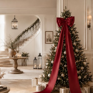 Könnte beinhalten: Ein hoher, üppiger grüner Weihnachtsbaum, geschmückt mit warmweißen Lichterketten und silbernen Kugeln, gekrönt von einer großen, tiefroten Satinschleife mit zwei langen, fließenden Bändern, die bis zum Boden herabhängen.