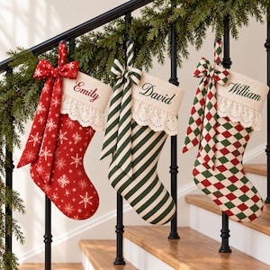 May include: Three Christmas stockings featuring cream-colored cuffs with eyelet lace trim and personalized embroidery. The first is red with white snowflakes, the second has green and white stripes, and the third features a red and green diamond pattern.