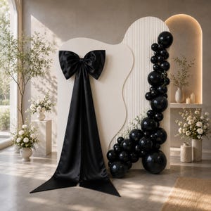 May include: A large black satin bow with long trailing ribbons attached to a cream-colored arched backdrop. A vertical cluster of glossy black balloons of varying sizes is arranged along the right side of the textured, wavy panel structure.