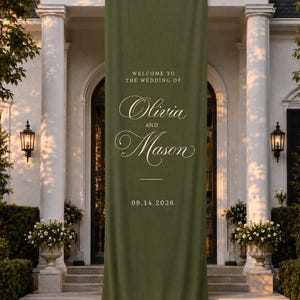 May include: A long, vertical olive green fabric banner featuring white text that reads "WELCOME TO THE WEDDING OF Olivia AND Mason 09.14.2026". The banner has a smooth, matte texture and hangs straight down, pooling slightly at the bottom on the ground.