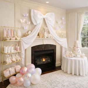 May include: A room decorated for a celebration, featuring a fireplace with a large white bow and draped fabric. A tiered cake and balloons are present. A gold shelving unit displays party favors.