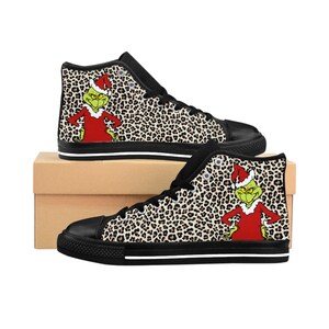 May include: High-top canvas sneakers with a black sole and a leopard print pattern. The sneakers feature a cartoon Grinch character in a Santa hat and red suit. The shoes are displayed on a brown cardboard box.