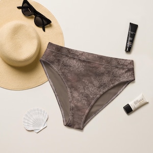 May include: Brown floral print underwear. The underwear is surrounded by a straw hat, sunglasses, a seashell, and two tubes of sunscreen. The underwear has a floral pattern in a lighter shade of brown.