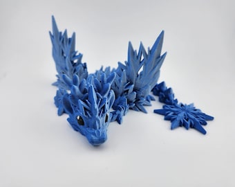 Könnte beinhalten: Eine blaue, 3D-gedruckte Drachenfigur mit einem stacheligen, eisigen Design. Der Drache hat einen langen Schwanz und Flügel, und seine Augen sind schwarz.