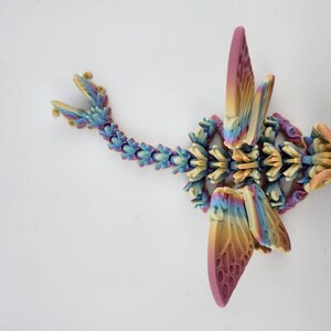 May include: A multi-colored 3D printed dragon figurine with wings, a tail, and a head. The dragon is made of plastic and has a rainbow color scheme.
