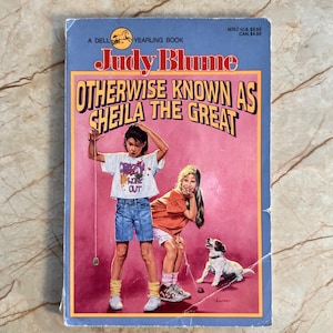 Peut inclure: Un livre de poche vintage intitulé "Otherwise Known as Sheila the Great" de Judy Blume. La couverture présente des illustrations de deux filles et d'un chien sur fond rose. Le livre est un Dell Yearling Book.