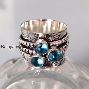 Może przedstawiać: Srebrny pierścionek obrotowy z trzema niebieskimi kamieniami szlachetnymi i wzorem kwiatowym. BalajiJewellersGifts.