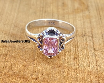 Peut inclure: Une bague en argent avec une pierre précieuse carrée rose sertie dans un décor en argent. La bague est marquée "925" à l'intérieur de la bande.