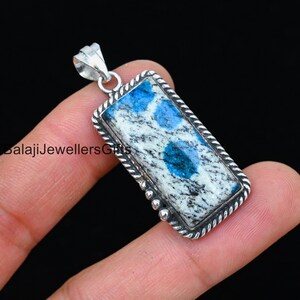Puede incluir: Un colgante de plata con una piedra azul y blanca. La piedra tiene forma rectangular y una superficie texturizada. El colgante está en una cadena de plata.
