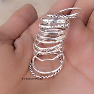 May include: A collection of silver rings in various designs, including twisted, patterned, and plain bands. The rings are stacked together, showcasing different textures and styles. The rings are displayed on a hand.