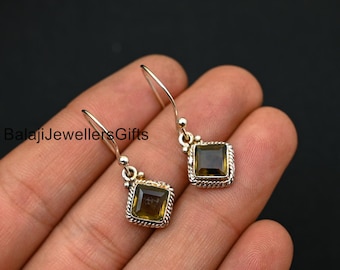 Puede incluir: Un par de pendientes colgantes de plata con piedras preciosas marrones de forma cuadrada. Los pendientes tienen un diseño delicado y son perfectos para el uso diario.