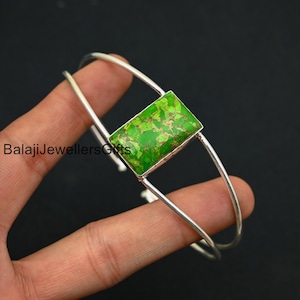 May include: A silver bangle bracelet with a green turquoise stone set in the center. The stone has a mottled green and gold pattern.