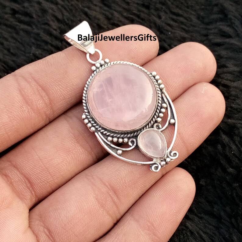 May include: A silver pendant featuring a large, round rose quartz and a smaller, teardrop-shaped stone. The pendant has decorative silver detailing and the text "BalajiJewellersGifts" is visible.