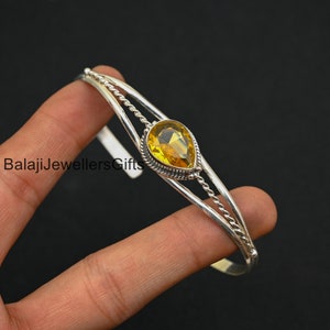 Op de afbeelding: Een zilveren armband met een gele edelsteen in het midden. De armband heeft een gedraaid draadontwerp.