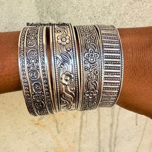 Könnte beinhalten: Ein Satz silberner Armreifen mit aufwendigen floralen und geometrischen Mustern. Die Armreifen sind gestapelt und zeigen detaillierte Designs und Texturen. Der Text "BalajiJewellersGifts" ist enthalten.