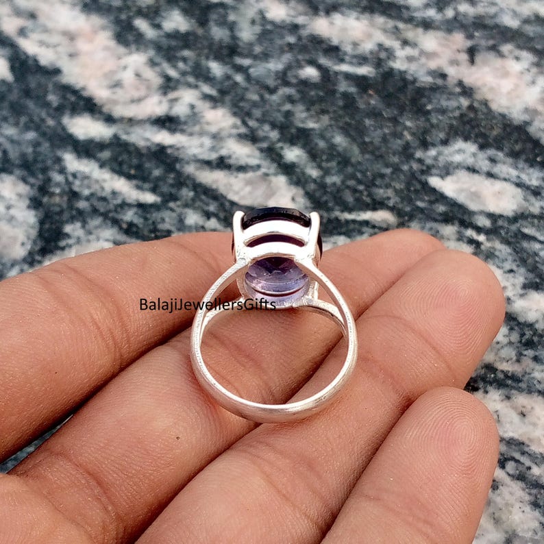 May include: A silver ring featuring a large, oval-cut amethyst gemstone. The amethyst has a deep purple hue at the top, fading to a lighter lavender color. The ring's band is a simple, polished silver design. The text "BalajiJewellersGifts" is visible.