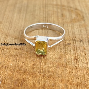 May include: A silver ring with a yellow gemstone set in a square shape. The ring has a split shank design.