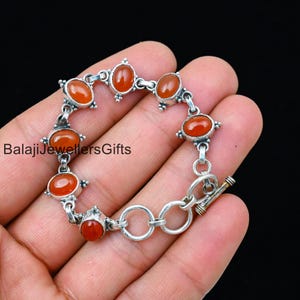 Puede incluir: Un brazalete de plata con cierre de palanca presenta piedras preciosas de cornalina. El brazalete tiene un total de siete piedras de cornalina de forma ovalada.