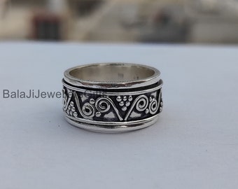 May include: A silver ring with a wide band and a decorative design of swirls and dots. The ring is made of sterling silver and has a polished finish.