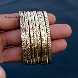 May include: A collection of gold-colored bangles with intricate floral and leaf patterns. The bangles are stacked together, showcasing detailed designs. The image includes the text "BalajiJewellersGift".
