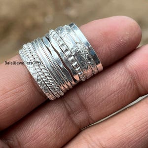 May include: A collection of silver rings with various textures and designs, including braided, hammered, and patterned surfaces. The rings are stacked on a finger, showcasing their different styles and details. The rings are from BalajiJewellersGifts.