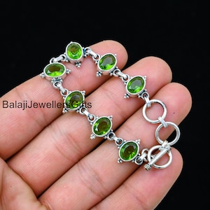 May include: A silver bracelet with green oval gemstones. The bracelet has a toggle clasp.