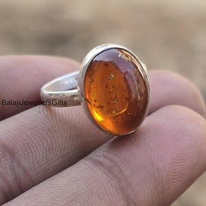 May include: A silver ring with an oval-shaped amber gemstone. The amber is a deep orange color with flecks of gold throughout.