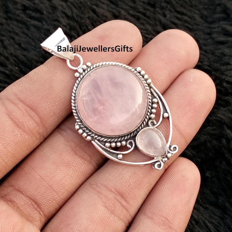 May include: A silver pendant featuring a large, round, pink rose quartz gemstone and a smaller, pear-shaped stone. The pendant has an intricate design and the text "BalajiJewellersGifts".