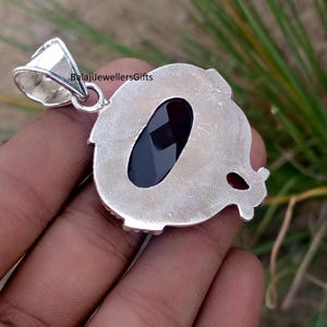 May include: A silver pendant with a large, oval, black gemstone at its center. The pendant has a decorative, textured border and a small loop for a chain. The text "BalajiJewellersGifts" is visible on the pendant.
