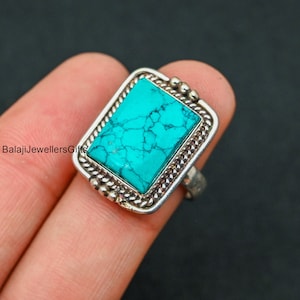 Peut inclure: Bague en argent ornée d'une pierre turquoise rectangulaire. La turquoise est d'un bleu-vert vif avec des veines sombres. La bague a une bordure décorative. Fond sombre.