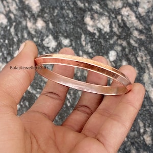 Op de afbeelding: Een koperkleurige armband met een geometrisch ontwerp. De armband heeft een platte boven- en onderkant met schuine zijkanten. Het oppervlak is glad en reflecterend, met de tekst "BalajiJewellersGifts" zichtbaar.