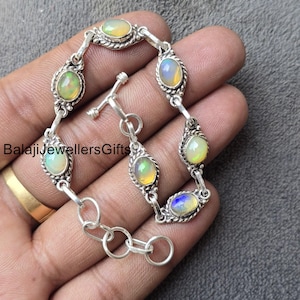 Puede incluir: Un brazalete de plata con cierre de palanca presenta seis piedras preciosas de ópalo de forma ovalada. Los ópalos son iridiscentes con tonos de verde, azul y amarillo.