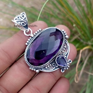 Puede incluir: Colgante de plata con una amatista púrpura oscura tallada en forma ovalada. Una amatista más pequeña, en forma de lágrima, está engastada debajo. El colgante tiene un diseño de filigrana y el texto "BalajiJewellersGifts".