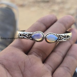 Puede incluir: Un brazalete de plata con dos piedras de ópalo en forma de lágrima. Las piedras son iridiscentes y presentan un arcoíris de colores.
