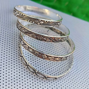 May include: Four silver bangles with floral designs. The bangles are stacked on top of each other.