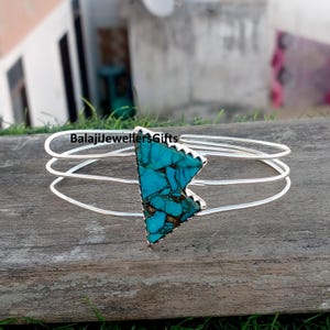 May include: A silver bracelet featuring a triangular turquoise stone. The stone is a vivid blue-green with brown veining. The bracelet has three parallel bands and the text "BalajiJewellersGifts".