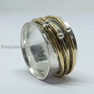 Può includere: Un anello girevole in argento e oro con tre bande d'oro e tre perle d'argento. L'anello è progettato per girare liberamente al dito.