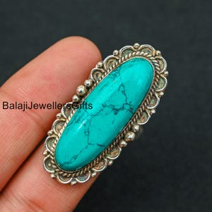 May include: A silver ring with a large oval turquoise gemstone. The ring has a detailed design with a rope-like border and small beads around the stone.